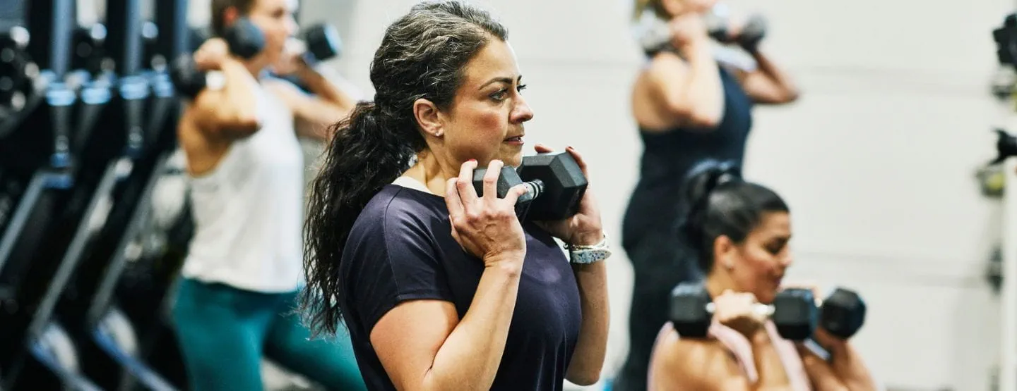 Woman doing dumbbell squats during fitness class in gym