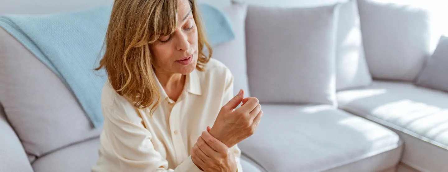Woman sitting on cough, gripping wrist in discomfort. 