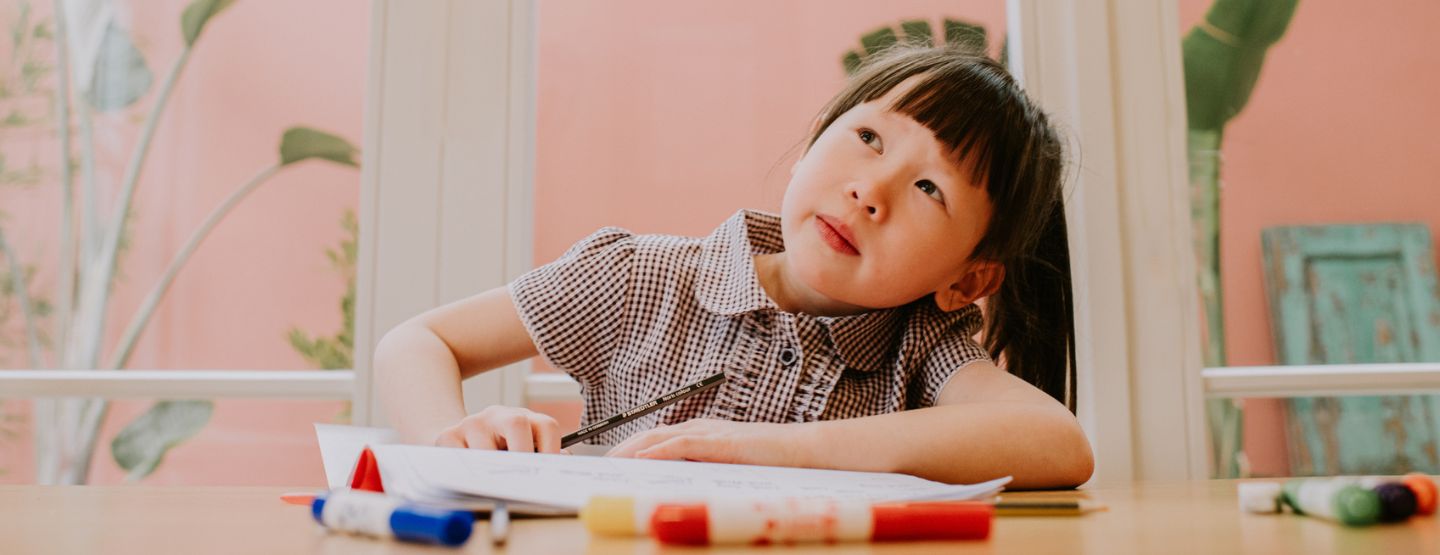 A little girl looks distracted as she stares off into space as she is supposed to be completing a homework assignment.