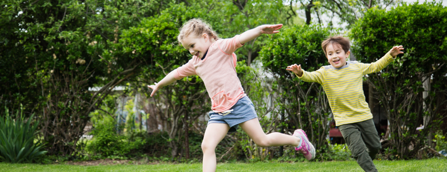A little boy and girl laughing and running around outside.
