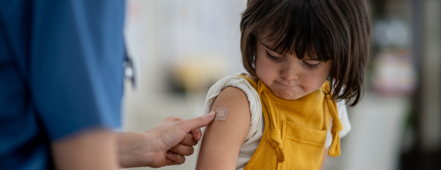 Young girl looks tentatively at band aid being put on her arm after a vaccination. 