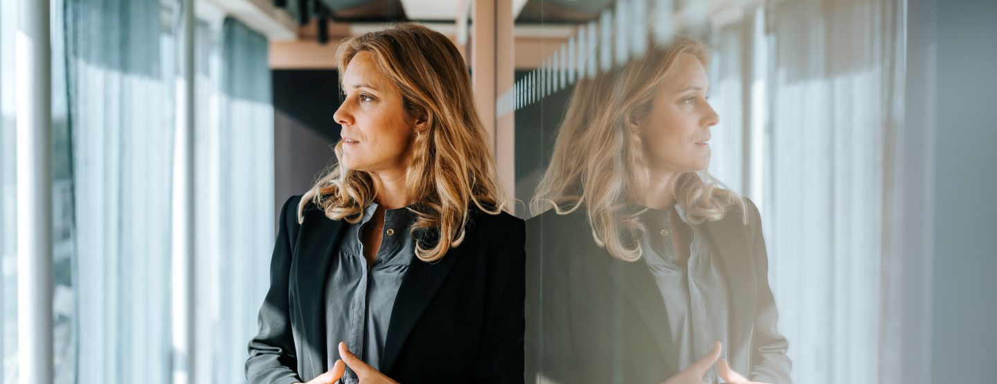 Professional woman leaning against wall looking worried. 
