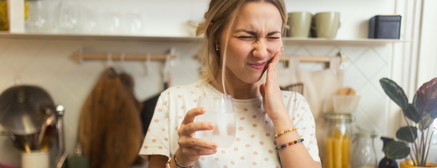 Woman grimacing and touching her teeth because of tooth pain.