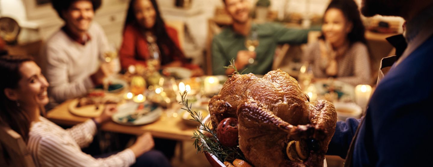 Close up of man serving roasted turkey during Thanksgiving dinner party with friends