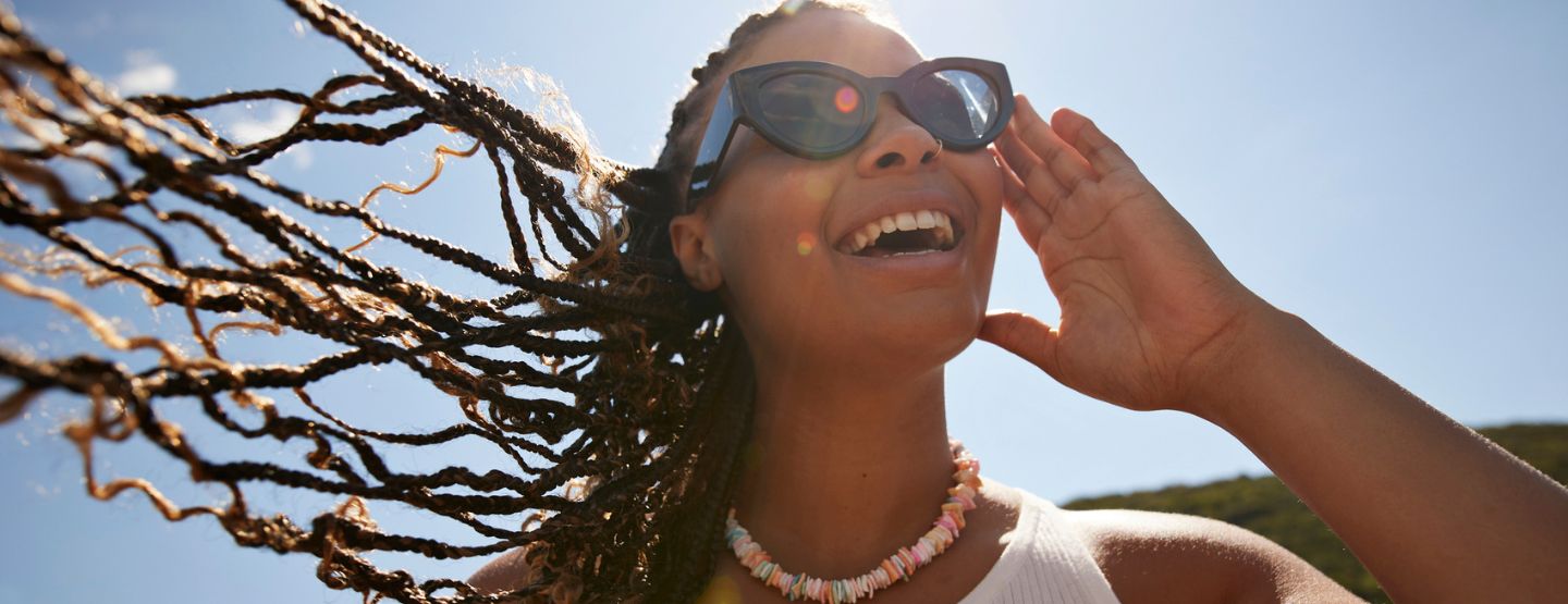 Woman wearing sunglasses smiling into the sun outside. 