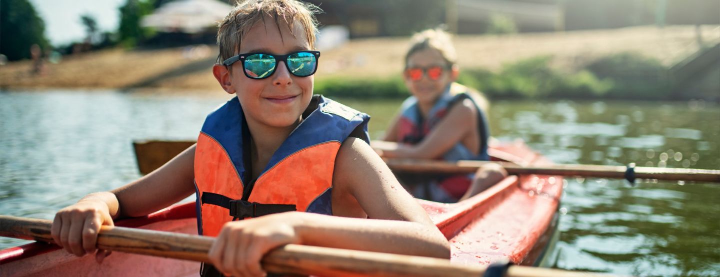Kids smiling wearing sunglasses while kayaking. 