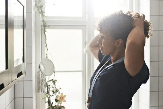 A female nurse ties her hair back in the mirror preparing for a day of work at ProMedica