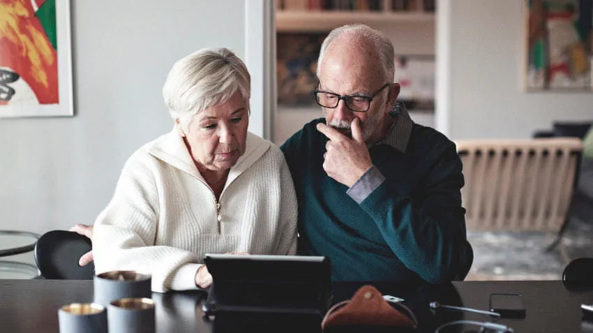 Senior couple sit at a table using a laptop 