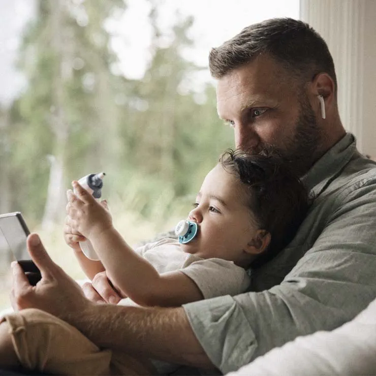 a father holds his toddler daughter during a telehealth visit with a doctor