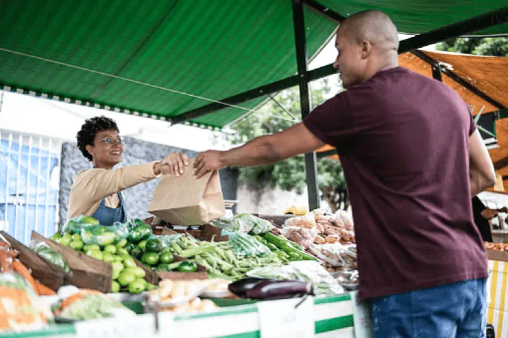 A young man buys produce from a female vendor at a farmer's market supporting community health