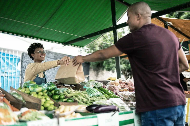 A man buys produce from a female vendor at a farmer's market supporting community health
