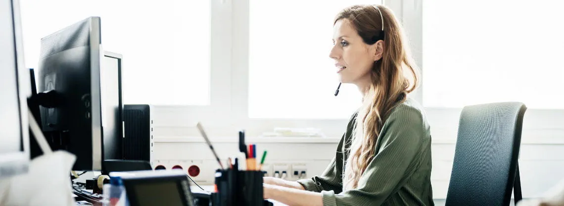 A woman at her work desk wearing a headset speaks to local media outlets