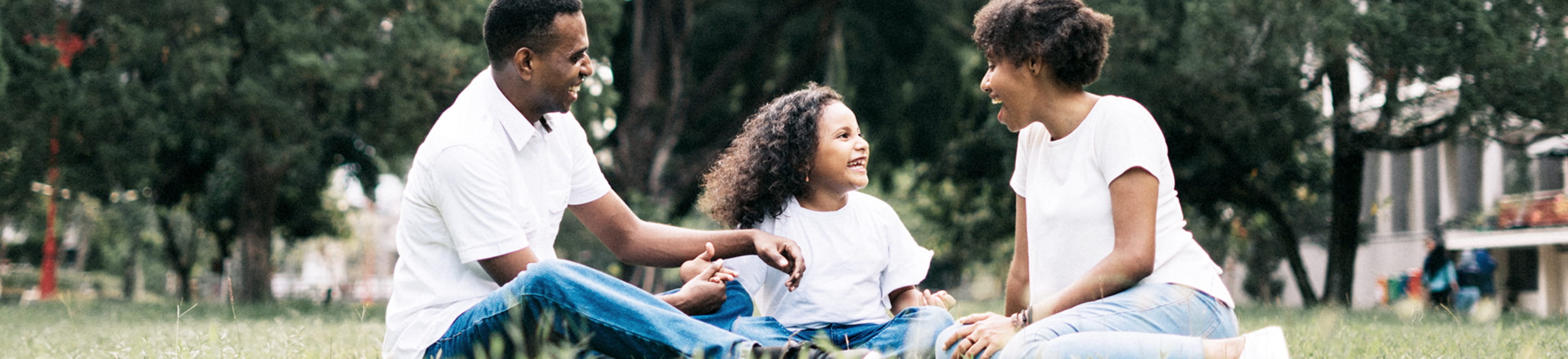 A family of three sit and laugh at a local park in their community