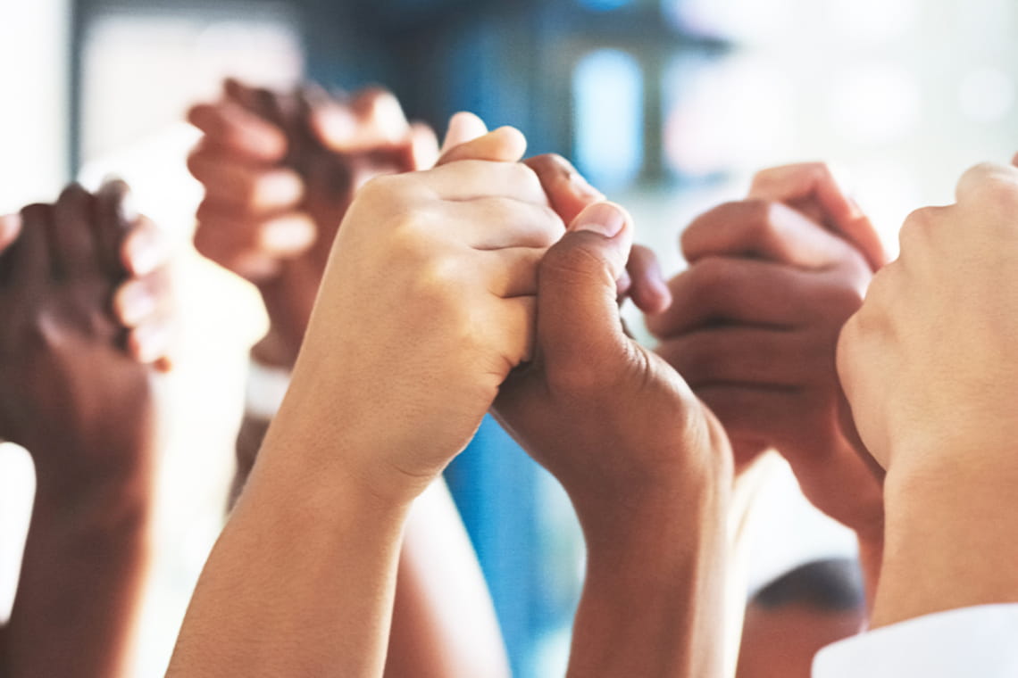 Hands from a volunteer group are being held in the air celebrating the conclusion of a successful community outreach program