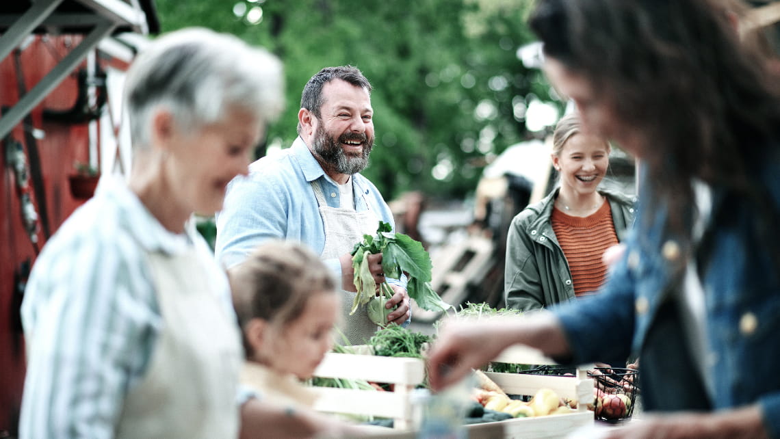 A man laughing and selling produce at a local farmers market organization