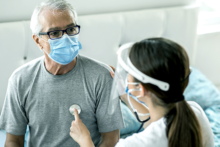 A masked senior man receives a home heart health visit from a masked doctor