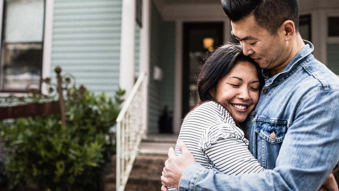 a couple hugs one another in front of the entrance of their home