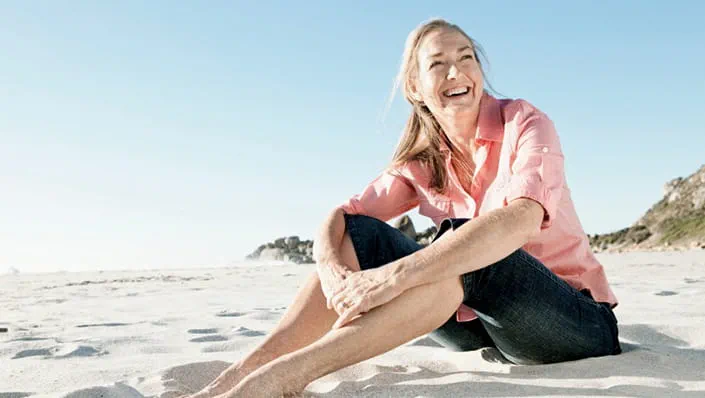 A smiling woman sits on the sand of a beach