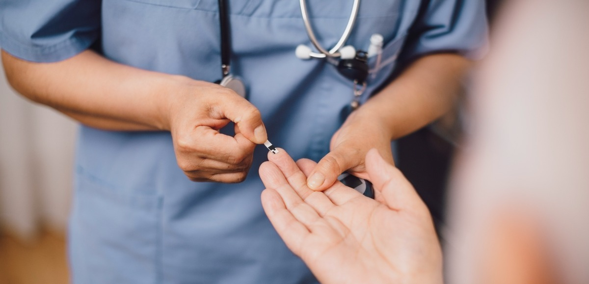 A close up of a nurse pricking a patients middle finger to get a blood sample.