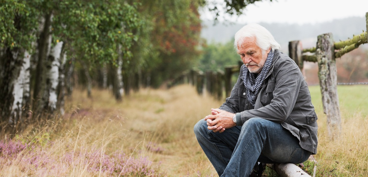 A broken hearted senior man sitting on a log.