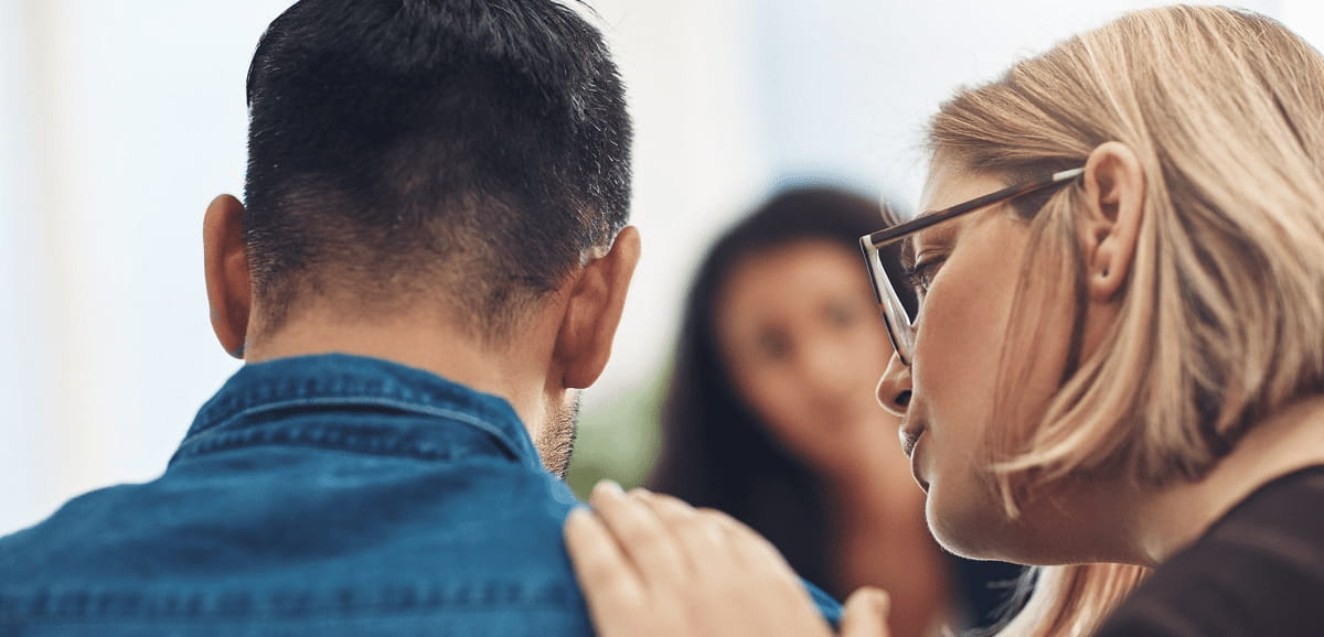 A woman with her hand on a mans shoulder while speaking to him.