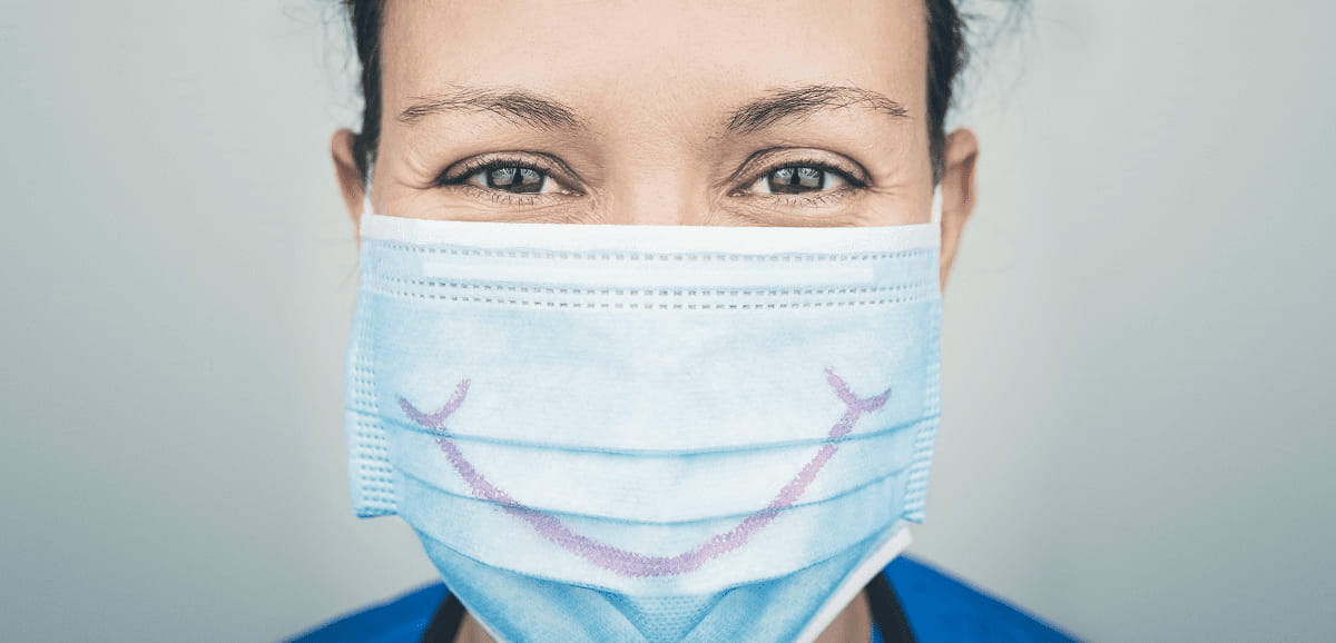 A healthcare worker wearing a face mask with a smile drawn on it.