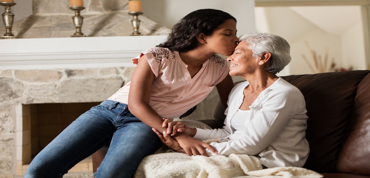 A young woman kissing the forehead of her senior mother.