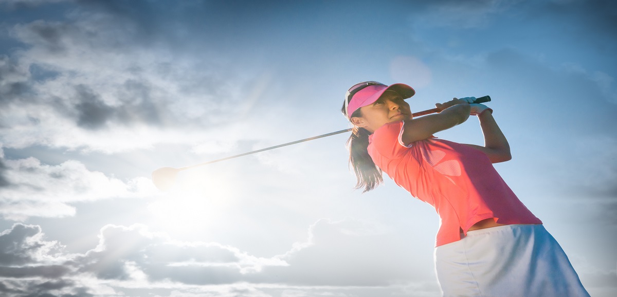 A women swinging at the golf ball on a beautiful course.