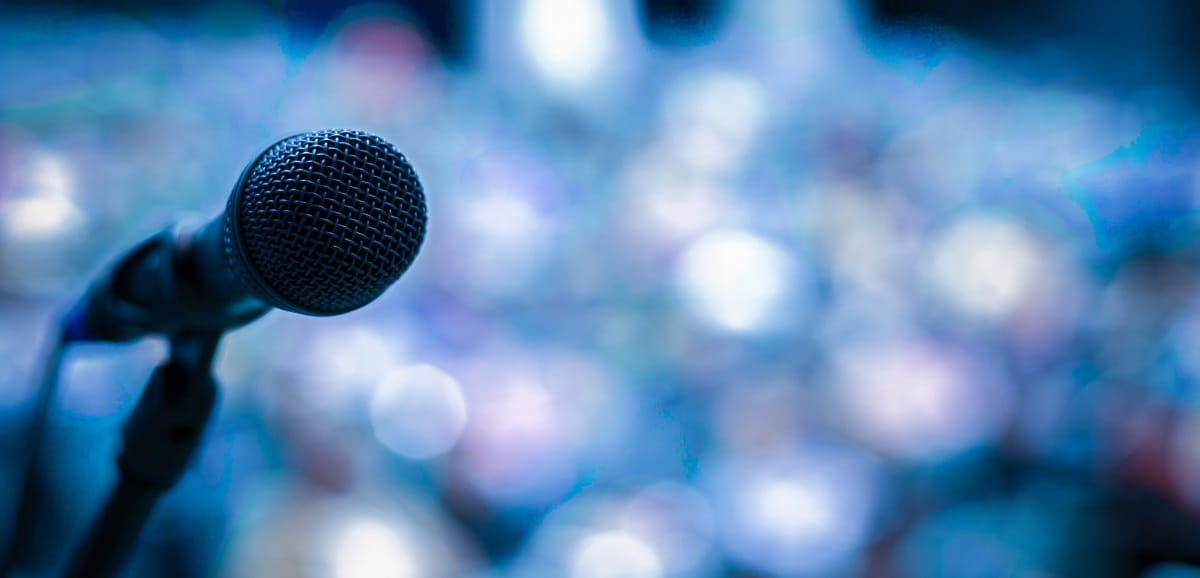 A close up of microphone on a stand with an out of focus crowd in the background.