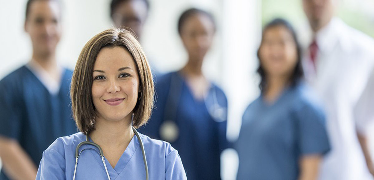 A female physician in the foreground with other male and female physicians behind her in the blurred background.