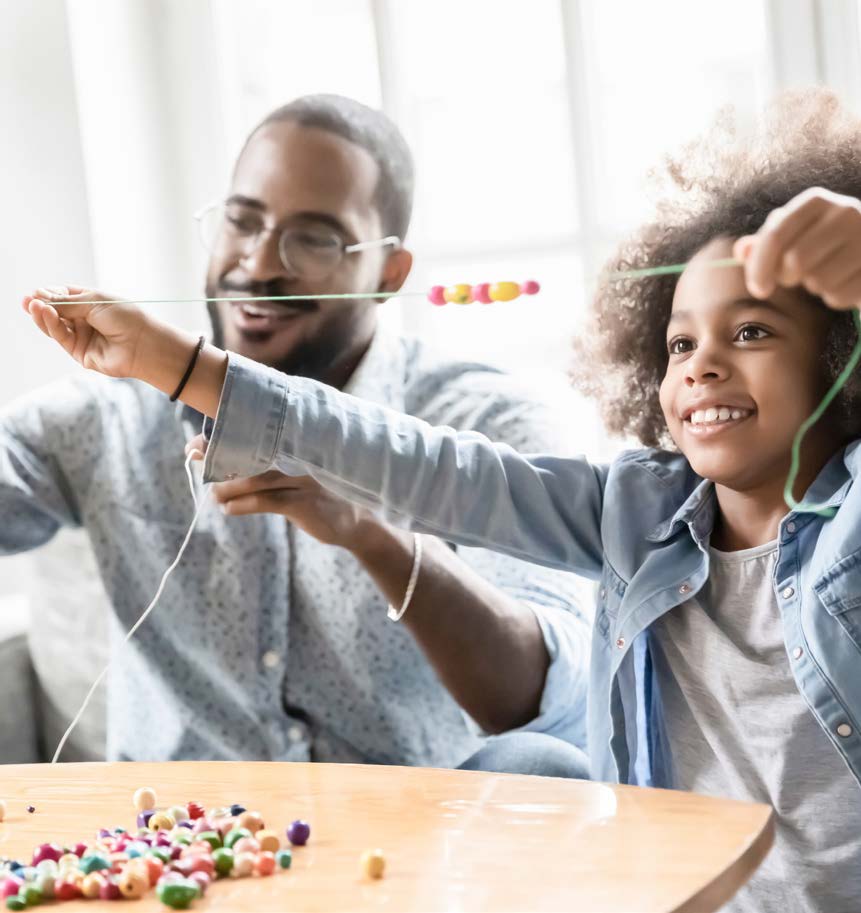 a father and child string beads together at a table