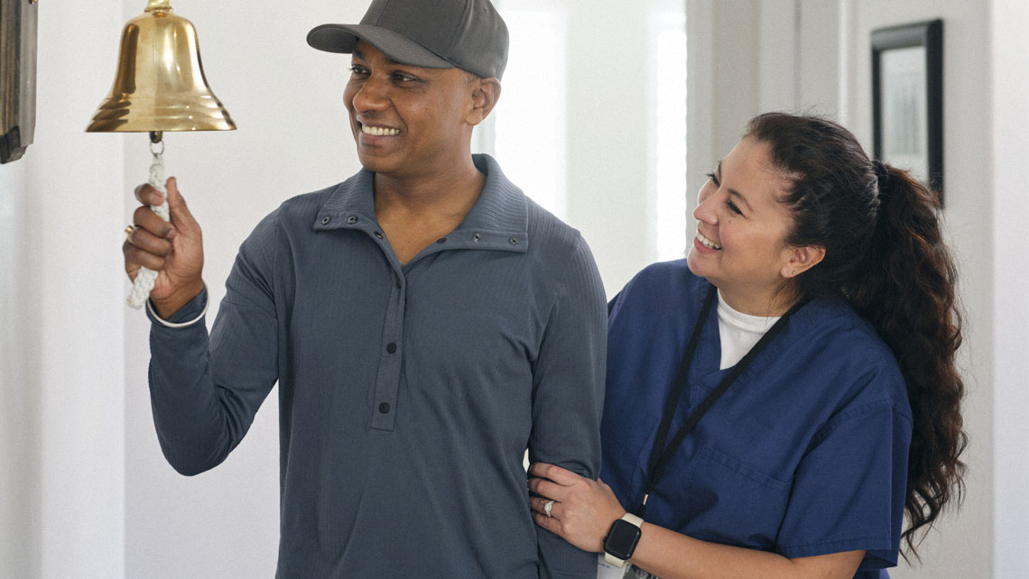 a patient who has just finished cancer treatment rings the office bell as his nurse looks on