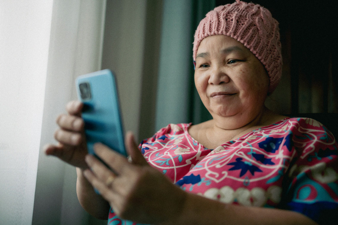 a woman wearing a colorful nightgown and stocking cap chats on a video call using her phone