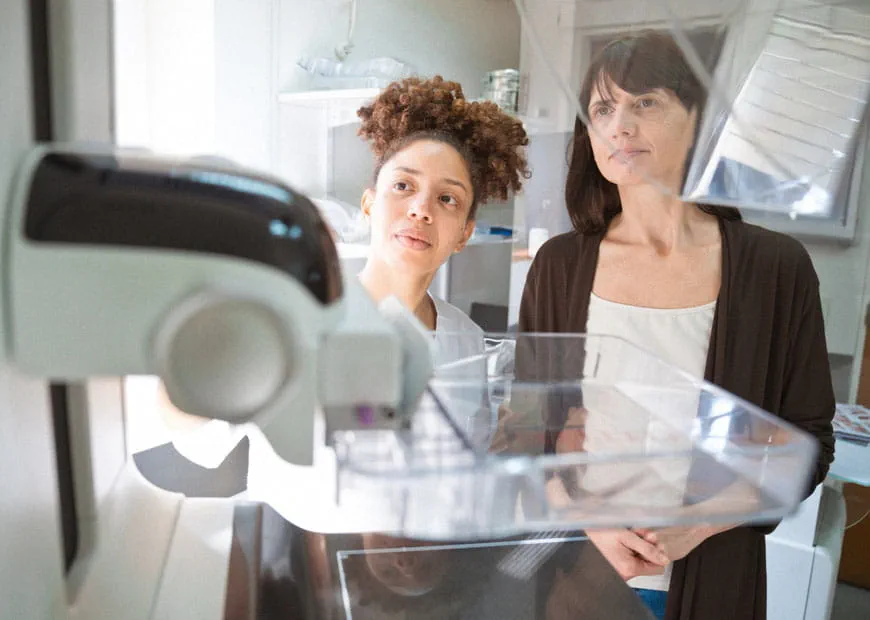 a radiology tech explains the mammogram machine to a patient