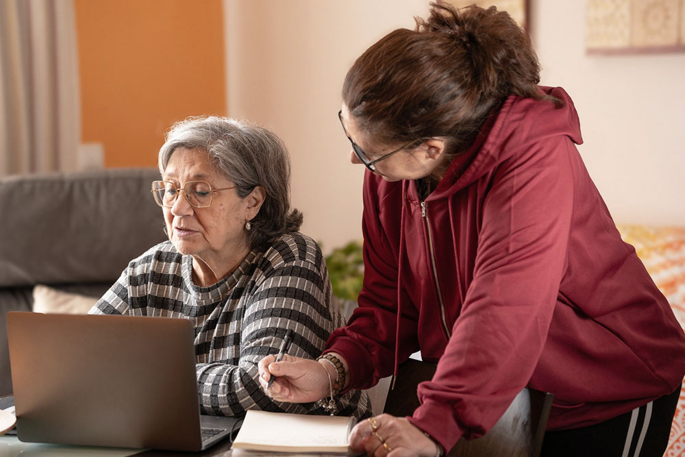 an adult woman and her senior mother look at a computer together